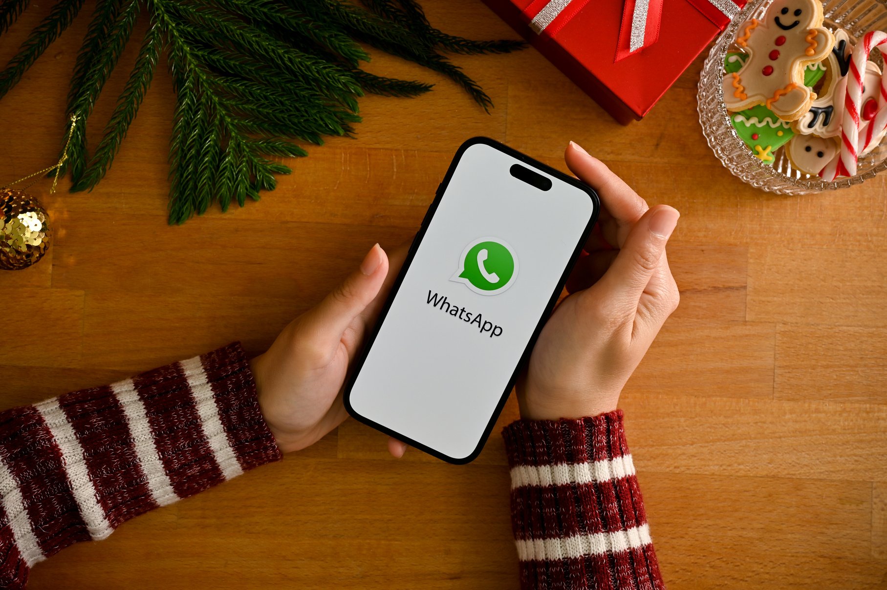 A female holding a smartphone with WhatsApp logo over wood table